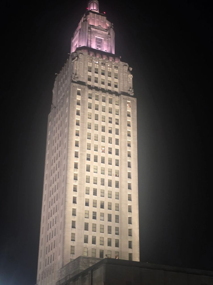 Tall, illuminated skyscraper with a pink-lit top against a dark night sky.