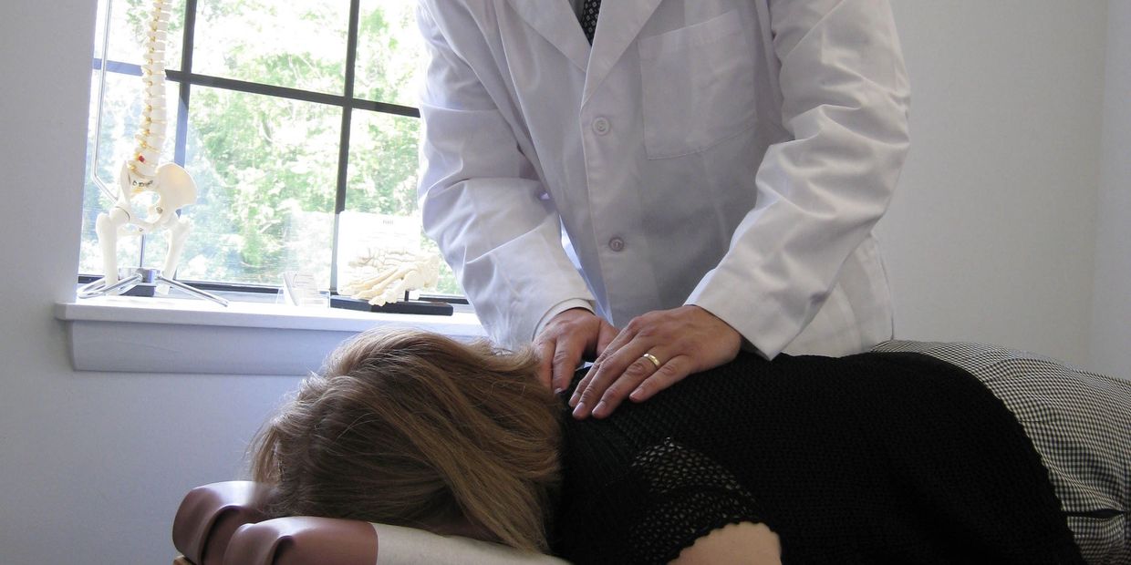 A chiropractor adjusts a patient's back in a clinic room with anatomical spine models.