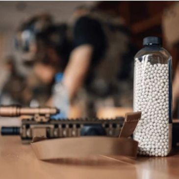 Bottle of white BB pellets next to a tactical rifle on a table.