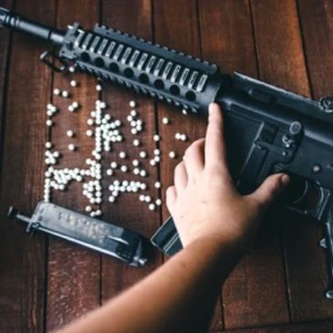 Hand holding an airsoft gun with BB pellets scattered on a wooden surface.