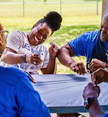 People laughing and playing a game at an outdoor picnic table.