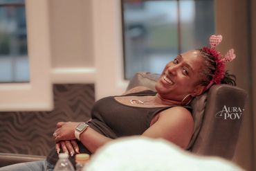 A woman smiling while reclining on a chair with heart-shaped headband.