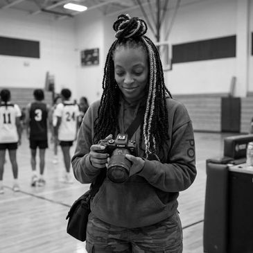 Woman with braided hair holding a camera in a gymnasium.