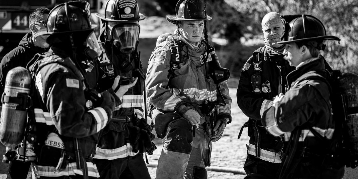 A group of firefighters in full gear having a serious discussion outdoors.