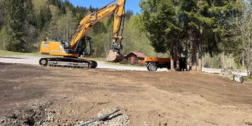 Ein Bagger arbeitet an einer Baustelle in einer Waldlandschaft.