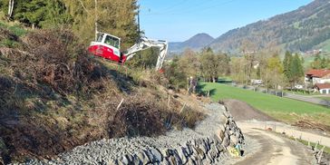 Bagger arbeitet an einer Böschung mit Steinmauer.