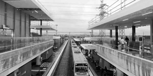 A train arriving at a modern elevated railway station on a cloudy day.
