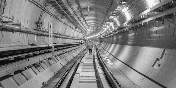 A worker in an orange vest walks inside a spacious, illuminated subway tunnel.