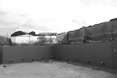 An empty, fenced outdoor space with covered structures and a dirt ground.