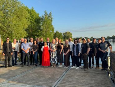 Group photo of people standing on a wooden bridge in a sunny outdoor setting.