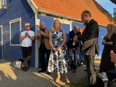 A group of people applauding a woman in a floral dress outside a blue house.