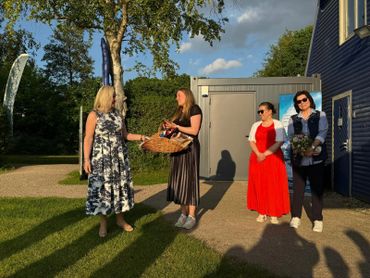 Four women outdoors exchanging a basket in warm sunlight.
