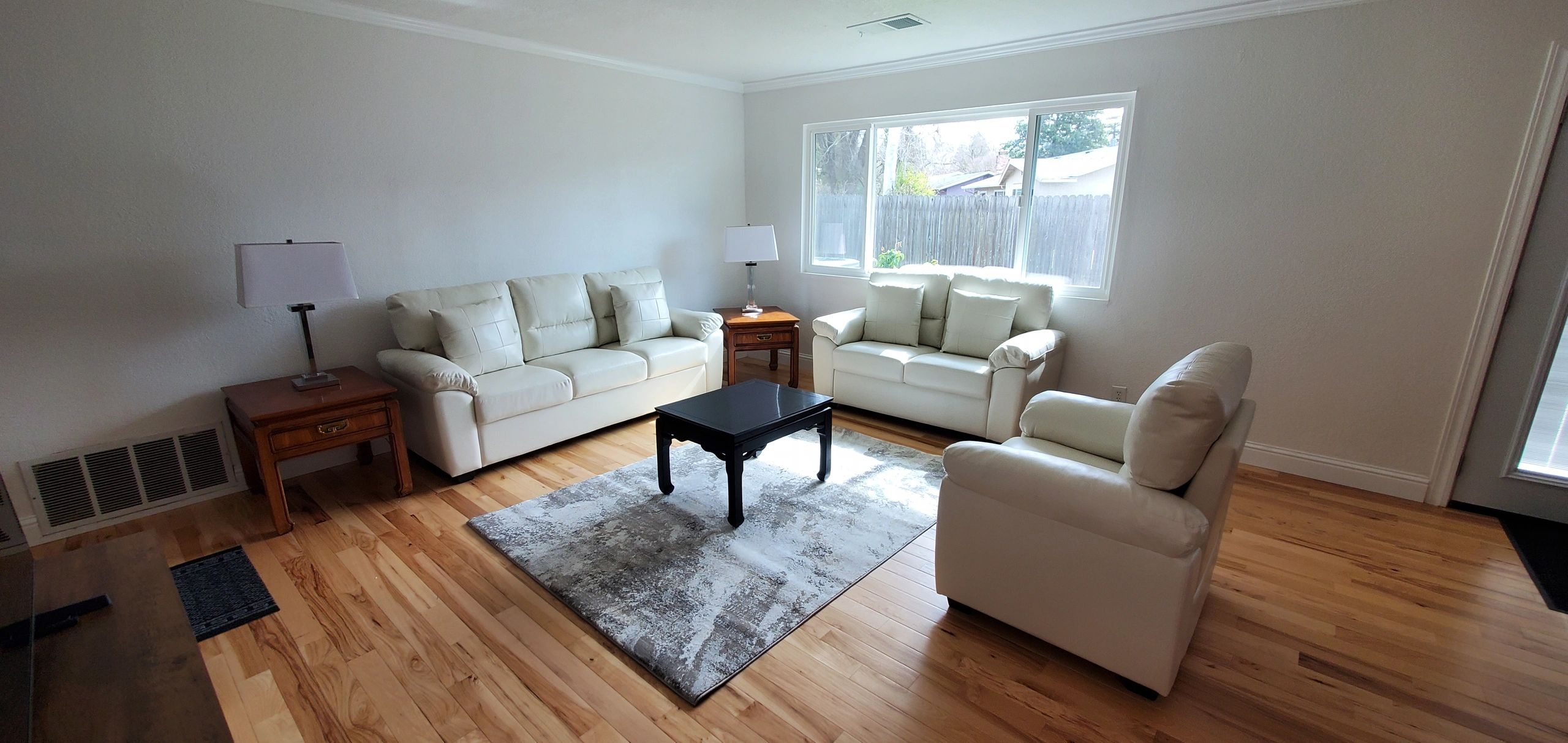 Bright living room with white sofas, wooden side tables, and a black coffee table on a patterned rug.