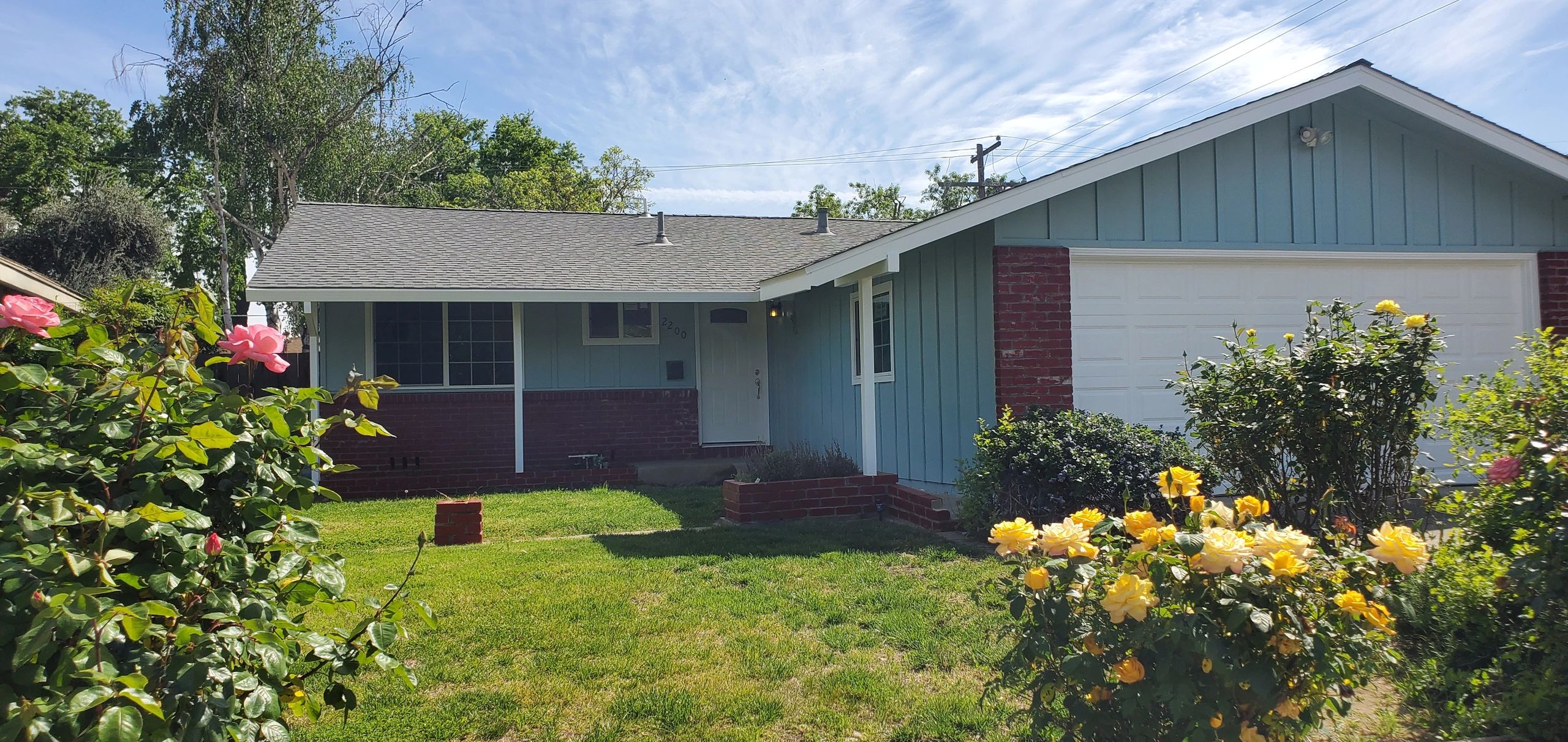 Single-story blue house with a well-kept garden and blooming flowers.