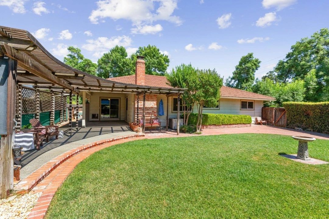 Sunny backyard with lush green lawn, patio seating, and wooden pergola.
