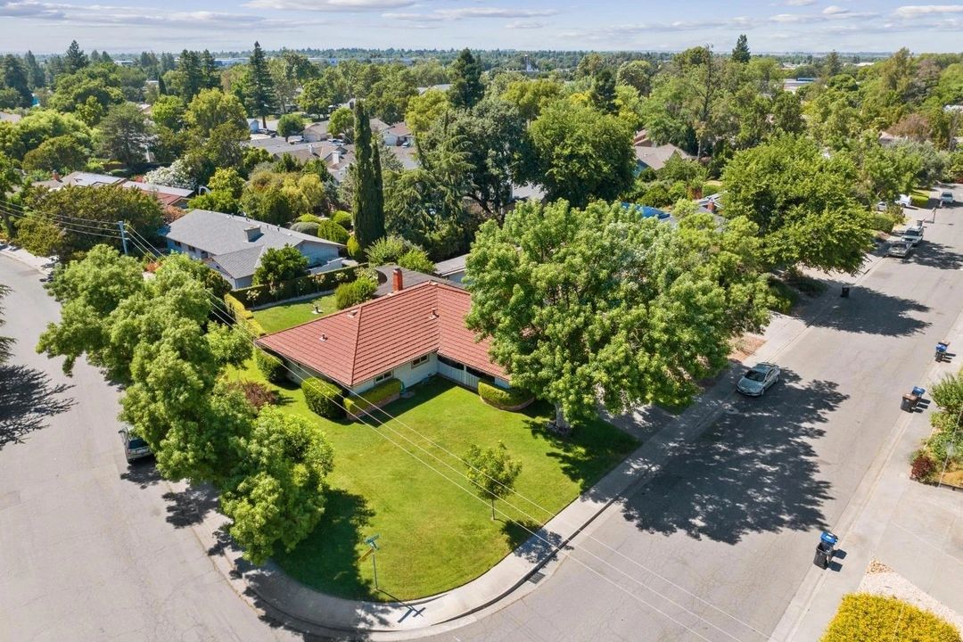A house with a red roof on a corner lot surrounded by lush green trees.