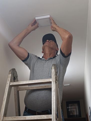 Man installing a ceiling light while standing on a ladder indoors.