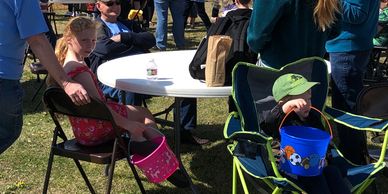 Children sitting outdoors with buckets at a table.