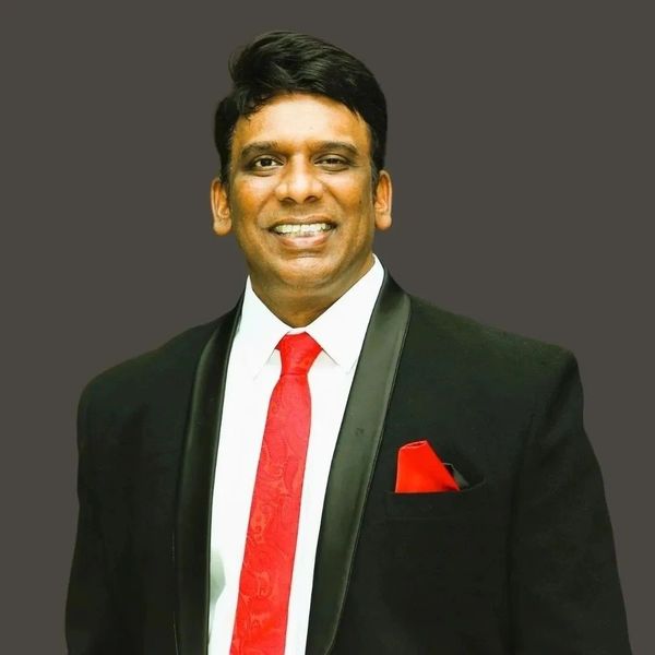Man in a black suit and red tie smiling.