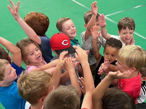 Group of children excitedly gathered around, raising hands and smiling.