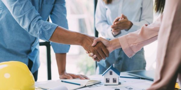 Two people shaking hands over a desk with a house model.