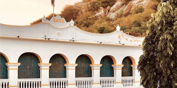 Historic white building with arches and green shutters under a hill.