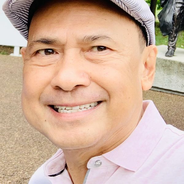 Smiling man wearing a striped cap and light pink shirt outdoors.