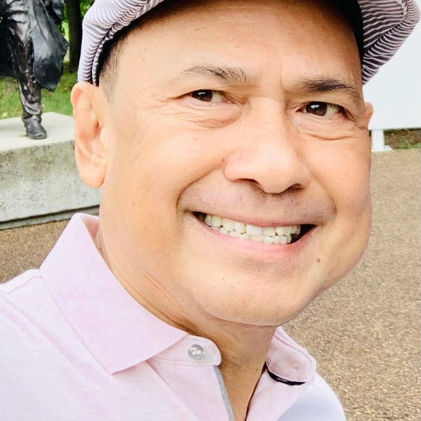 Smiling man wearing a striped cap and pink shirt outdoors.