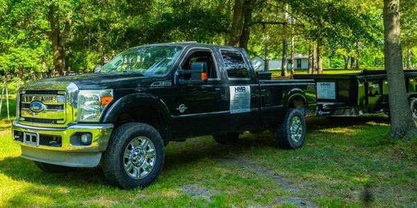 Black Ford pickup truck parked in a wooded area with a trailer attached.