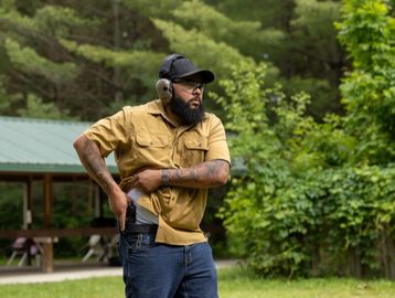 Man practicing drawing a handgun outdoors with hearing protection.