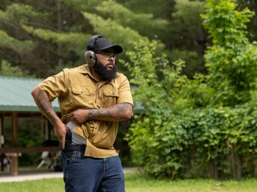 Man practicing drawing a handgun outdoors with hearing protection.