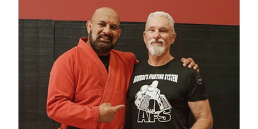 Two men posing in martial arts attire, one in a red gi and the other in a black t-shirt.