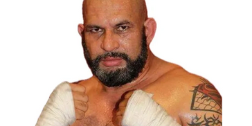 Muscular bald man with a beard and wrapped hands posing for a photo.