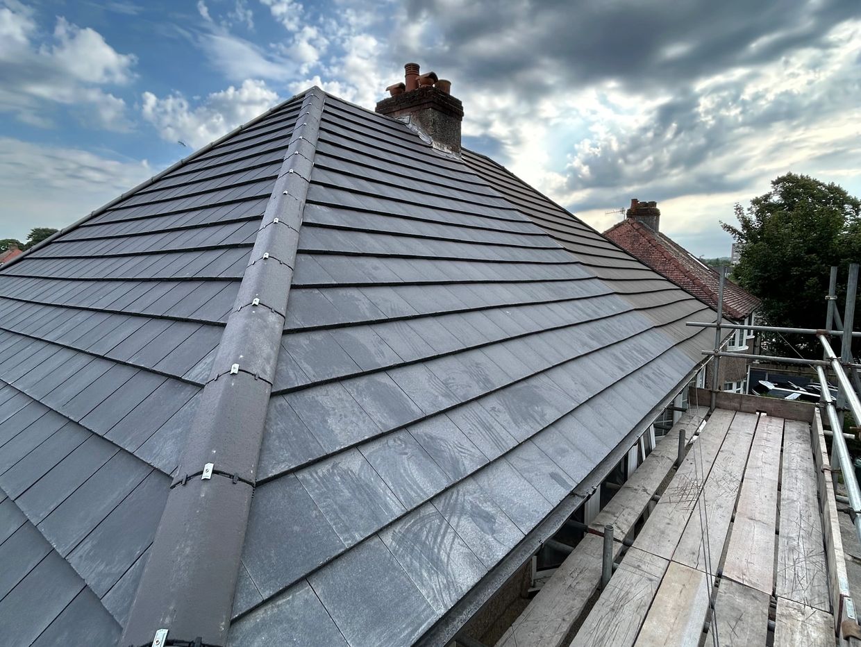 Newly tiled slate roof with a chimney under a cloudy sky.