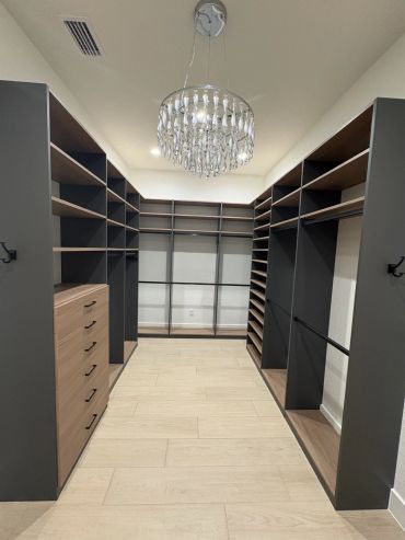 Modern walk-in closet with dark shelves and chandelier.