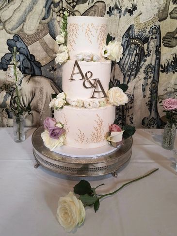 Elegant three-tier wedding cake adorned with flowers and initials A&amp;A.
