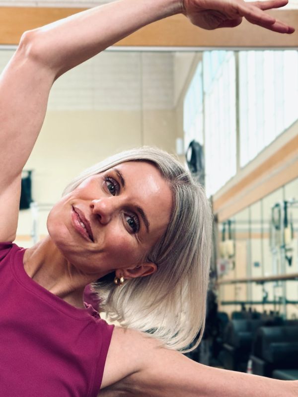 A smiling woman stretching in a gym.