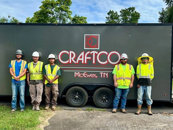 Five construction workers in safety gear standing by a trailer.