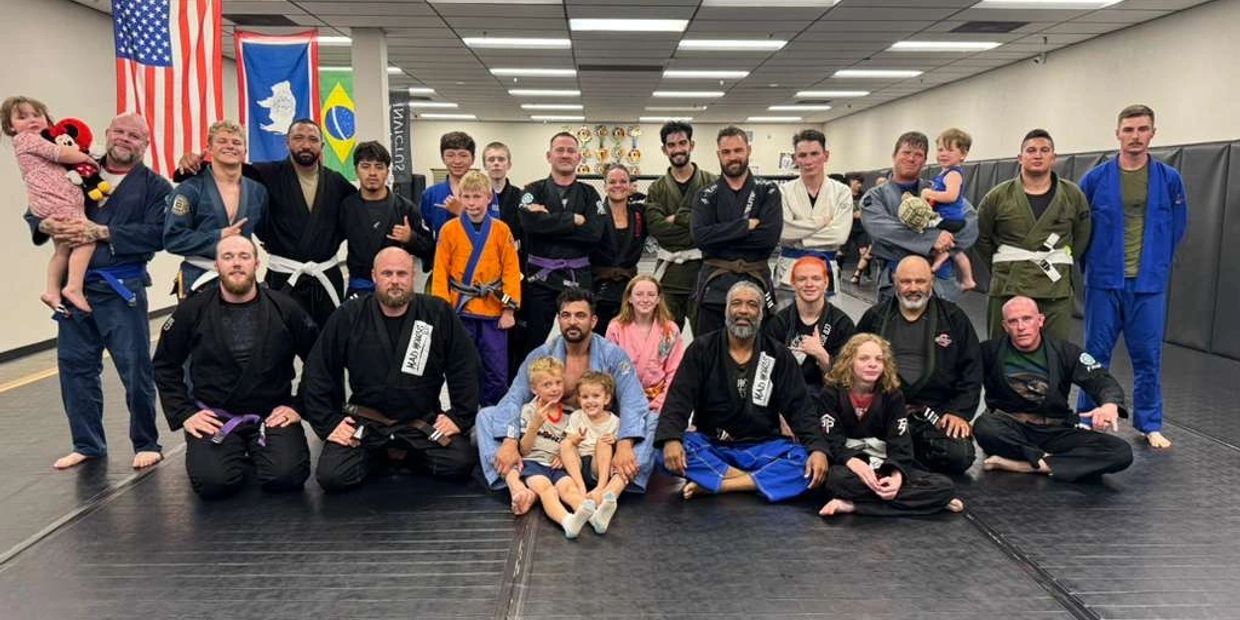 A diverse group of martial artists and children posing in a gym with flags in the background.