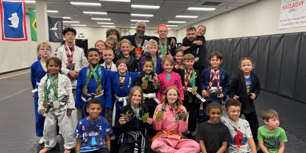 Group of kids and instructors posing with medals in a martial arts gym.