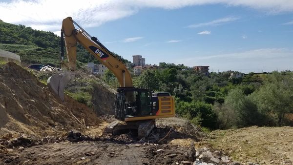 Yellow Caterpillar excavator digging on a construction site with a mountainous background.