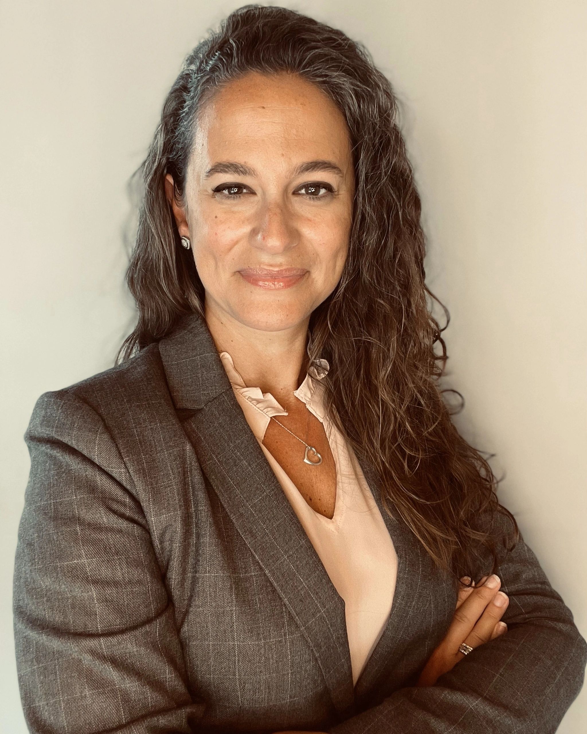 Professional woman with long curly hair wearing a blazer and heart necklace.