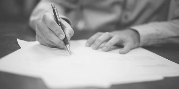 Image of a person's hands with a pen writing on a piece of paper