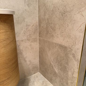 Corner of a bathroom with beige stone tiles and wooden accent.