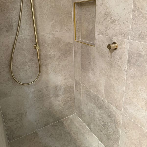 Modern shower with beige tiles and brass fixtures.