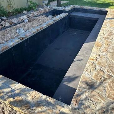 Empty rectangular garden pond with stone edges and gravel bed.