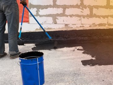Person applying black waterproof coating on concrete floor with roller.