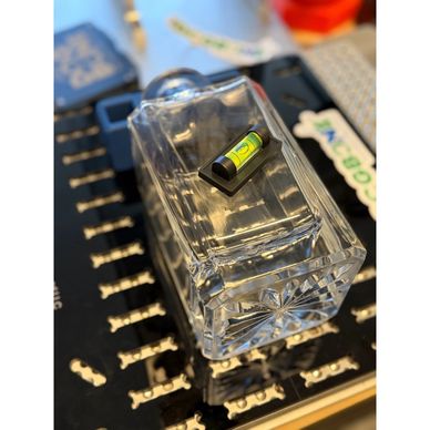 A small spirit level placed on a clear glass rectangular object on a cluttered surface.