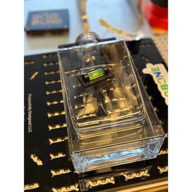 A small vial with green liquid inside a clear plastic container.