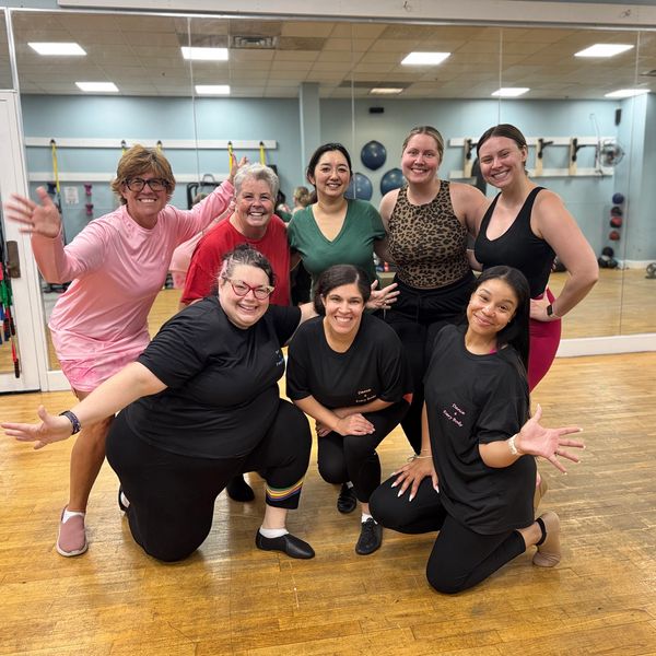 Group of eight women smiling and posing in a gym studio.